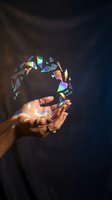 Close-up of a woman's hand holding iridescent crystal shards floating above her palm against dark background. Colorful light refraction creates rainbow effects for creative and spiritual concepts.