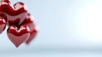 Glossy red heart shapes floating against soft white background, creating romantic atmosphere for Valentine's Day designs or love-themed projects.