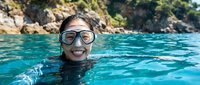 Happy young woman snorkeling in crystal clear turquoise water wearing diving mask and smiling at camera during tropical vacation adventure.