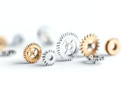 Metallic silver and gold colored gears arranged in line on white background with selective focus and shallow depth of field, showing mechanical precision.