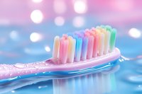Colorful toothbrush with rainbow bristles on wet surface against blurred pastel background, representing dental hygiene and oral care.