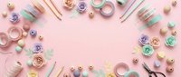 Flat lay crafting supplies frame on pink background with paper flowers, ribbons, scissors and decorative elements for DIY projects and scrapbooking.