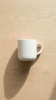 White ceramic mug on light wood surface with shadow, suitable for beverage branding, mockup designs, and product presentations.