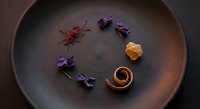 Gourmet chocolate dessert with edible flowers and saffron on dark ceramic plate. Fine dining presentation for luxury restaurant menu and culinary arts.