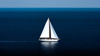 Lone white sailboat with raised sails gliding across deep blue ocean waters under clear sky, creating minimalist nautical scene for luxury travel and adventure.