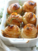 Roasted onion roses garnished with fresh thyme in white ceramic baking dish. Golden caramelized layers create elegant spiral pattern, seasoned with herbs and spices.