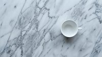 White ceramic cup on marble surface with veining pattern, overhead view for minimalist design, interior styling, and product photography projects.