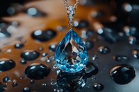 Teardrop blue topaz pendant necklace with diamond accent on reflective surface surrounded by water drops, luxury jewelry macro photography.