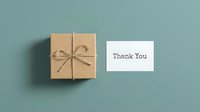 Kraft paper gift box tied with twine bow beside a thank you card on a muted teal background, perfect for gratitude and gifting concepts.