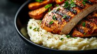 Grilled sausages with creamy mashed potatoes and roasted carrots on dark plate. Comfort food dinner with herbs and spices for restaurant menu design.