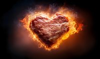 Heart-shaped raw meat steak engulfed in bright orange flames against dark background, symbolizing passion for grilling and cooking.