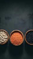 Wooden bowls filled with white beans, red lentils, and black beans arranged on dark slate background for cooking and nutrition content.