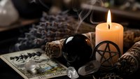Mystical altar setup with burning candle, crystal ball, tarot cards, sage bundles and pentagram symbol for spiritual divination and witchcraft practices.