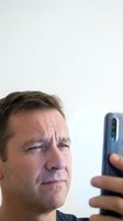 Middle-aged Caucasian man with concerned expression looking at smartphone screen, showing digital stress and technology anxiety in modern lifestyle.