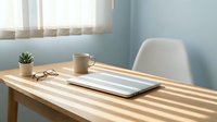 Wooden desk with laptop, coffee mug, eyeglasses and small succulent plant in bright sunlit workspace with blue wall and white chair.