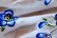 Delicate blue floral embroidery pattern on white fabric with intricate stitching detail and soft selective focus creating dreamy textile background.