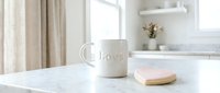 White ceramic mug with love inscription beside a pink heart-shaped cookie on marble countertop in bright minimalist kitchen interior.