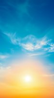 Vibrant sunset sky with bright sun and wispy cirrus clouds creating dramatic atmosphere against gradient from deep blue to warm orange and yellow horizon.