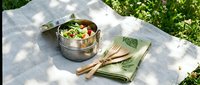 Healthy lunch in stainless steel container on checkered blanket outdoors. Fresh salad with vegetables in metal lunchbox for picnic dining and sustainable eating.