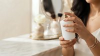 Woman with medium skin tone holding white cosmetic jar, displaying manicured nails and gold ring. Skincare product application for beauty, wellness, and cosmetics marketing.