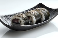 Fresh sushi rolls with sesame seeds served on curved black ceramic plate against white background. Traditional Japanese cuisine presentation.