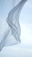 Flowing translucent blue fabric in motion against white background creating elegant waves and curves for fashion and textile design projects.