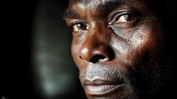Close up portrait of African man's face in dramatic lighting showing intense gaze and strong facial features against dark background, artistic emotional photography.