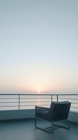 Modern lounge chair on waterfront deck at sunrise, overlooking calm lake with metal railing. Serene morning atmosphere for relaxation and contemplation spaces.