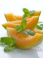 Fresh cantaloupe melon slices garnished with mint leaves on white background, showcasing juicy orange flesh and green rind for food photography.