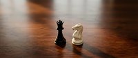 Black king and white knight chess pieces facing each other on wooden board representing strategic business competition and tactical planning.