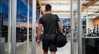 Athletic man entering modern gym facility carrying sports bag during evening workout session for fitness and health goals.