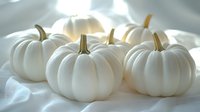 White decorative pumpkins on soft fabric with natural lighting creating gentle shadows. Elegant autumn decor for modern seasonal styling and festive arrangements.