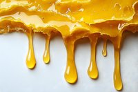 Golden honey drips and drizzles creating natural organic patterns against white background, showing viscous liquid texture and flow in macro photography.