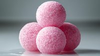 Pink sugar-coated candy balls stacked in a pyramid formation against a neutral background, showcasing their textured, crystalline surface.