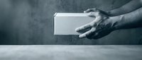 Male hands holding white blank box package against concrete wall background for product presentation and mockup design purposes.
