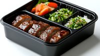 Grilled teriyaki chicken in black bento box with steamed broccoli and fresh carrots. Traditional Japanese lunch meal with protein and vegetables served in compartments.
