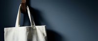 Natural cotton tote bag hanging on wooden hook against dark blue wall. Eco-friendly reusable shopping bag mockup for branding and sustainable lifestyle concepts.