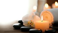 Spa wellness scene with burning candle, orchid flower and hot stones creating peaceful atmosphere for relaxation and massage therapy treatments.