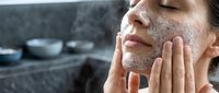 Young woman applying exfoliating scrub to face in modern bathroom, skincare routine, facial treatment, beauty wellness self-care ritual.