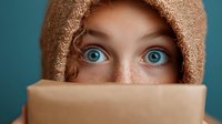 Young woman with striking blue eyes and freckles partially hidden behind beige scarf against turquoise background, expressing mystery and intrigue through intense gaze.