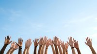 Diverse group of raised hands against clear blue sky, representing unity, teamwork, community support, and collective action for volunteer work or charitable causes.