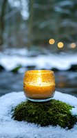 Golden textured glass candle holder glowing warmly on moss-covered stone in snowy winter garden with soft bokeh lights creating cozy atmosphere.