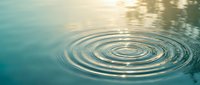 Concentric water ripples spreading across calm turquoise surface with golden sunlight reflections creating peaceful zen meditation atmosphere for wellness concepts.