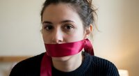 Young woman with red cloth covering mouth symbolizing censorship, silence, and freedom of speech restrictions in modern society.