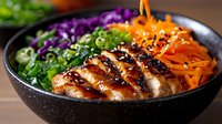 Grilled teriyaki chicken bowl with colorful vegetables, shredded carrots, purple cabbage, green onions and black sesame seeds served in dark ceramic bowl.