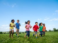 Diverse group of children running together across green meadow on sunny day, wearing colorful casual clothing. Outdoor activity for kids, summer recreation, and friendship concepts.