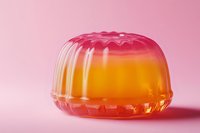Colorful layered jelly dessert with orange and pink gradient colors on pink background, soft lighting creates appetizing translucent effect and subtle shadow.