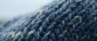 Blue knitted wool fabric texture with detailed stitching pattern showing soft yarn fibers and craftsmanship for cozy winter clothing and textile projects.