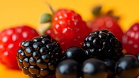 Fresh mixed berries including ripe blackberries, red raspberries and blueberries on warm yellow background for healthy eating and nutrition concepts.