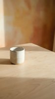 Minimalist white ceramic mug on wooden table with warm sunlight and blurred terracotta wall background, suitable for product photography and lifestyle design.